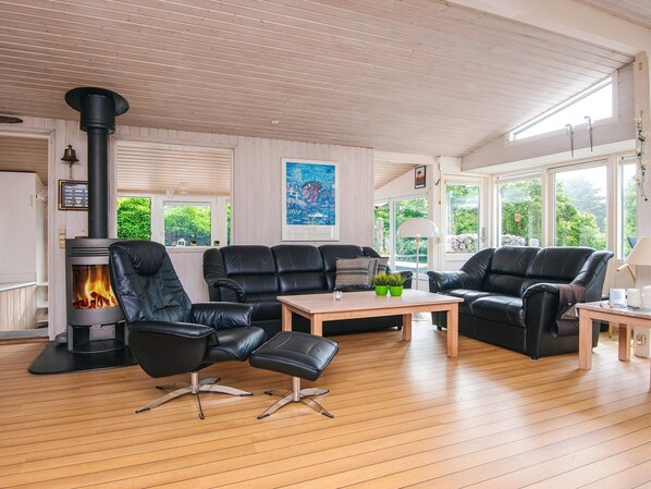 A cozy living room with a black leather sofa set, a wooden coffee table, and a wood-burning stove.