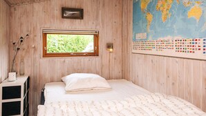 A wooden room with a bed, a window, a map, and a small shelf with a vase.