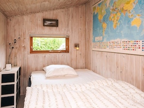 A wooden room with a bed, a window, a map, and a small shelf with a vase. - 4 Star Holiday Home in Lokken (Lokken)