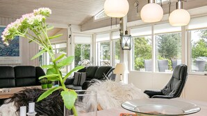 A modern living room with a glass coffee table, a black leather sofa, and a dining table with a floral placemat.