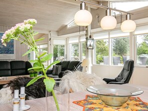 A modern living room with a glass coffee table, a black leather sofa, and a dining table with a floral placemat. - 4 Star Holiday Home in Lokken (Lokken)