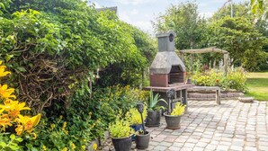 A garden with a stone barbecue grill, potted plants, and a paved walkway.