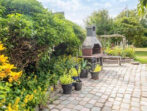 A garden with a stone barbecue grill, potted plants, and a paved walkway. - 4 Star Holiday Home in Lokken (Lokken)