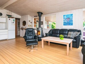A cozy living room with a black leather sofa, a wooden coffee table, a black leather chair, and a wood-burning stove. - 4 Star Holiday Home in Lokken (Lokken)