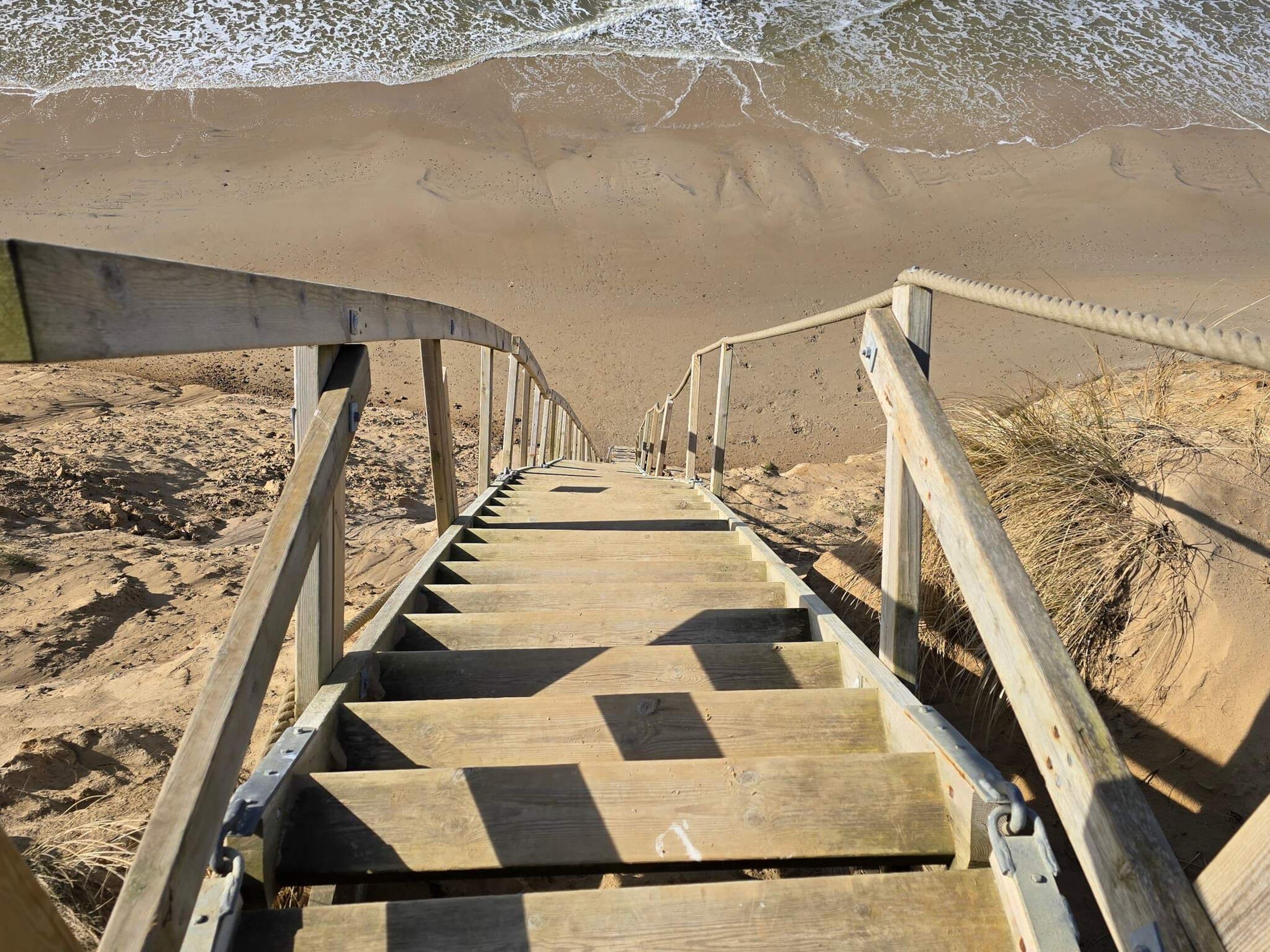 Una escalera de madera que conduce a una playa, con barandilla a ambos lados.