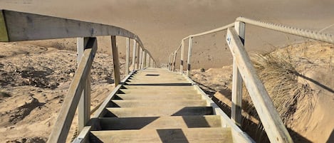 Una escalera de madera que conduce a una playa, con barandilla a ambos lados.