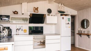 A modern kitchen with white cabinetry, a built-in oven, and a refrigerator. There is a wooden floor and a clock on the wall.