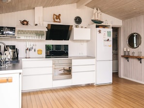 A modern kitchen with white cabinetry, a built-in oven, and a refrigerator. There is a wooden floor and a clock on the wall. - 4 Star Holiday Home in Lokken (Lokken)