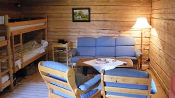 Interior de una cabaña con literas, un sofá, una mesa y una lámpara.