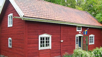 Un edificio rojo de madera con techo inclinado, una puerta con ventana y una bandera.