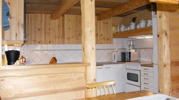Un interior de madera con una zona de cocina, que incluye armarios, una estufa y una mesa de comedor con una silla.