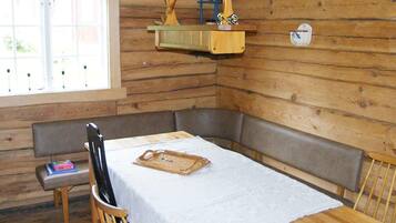A wooden cabin interior with a dining table, benches, and a hanging light fixture.