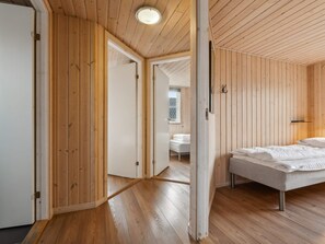 A modern bedroom with wooden paneling, a bed with white bedding, and a visible bathroom with a white sink and mirror. - 5 Star Holiday Home in Bagenkop (Sydlangeland)