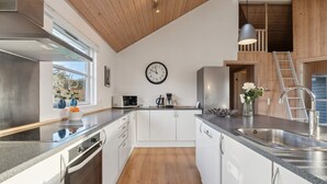 A modern kitchen with white cabinets, stainless steel appliances, a wooden ceiling, and a large window providing natural light. - 5 Star Holiday Home in Bagenkop (Sydlangeland)