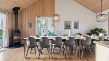 Een moderne eetruimte met een houten plafond, een ingebouwde houtkachel en een groot raam.
