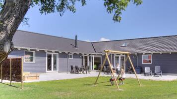A residential building with a patio area, outdoor seating, and a swing set.
