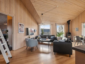A modern living room with wooden walls, a flat-screen TV, a fireplace, and a dining area with chairs.