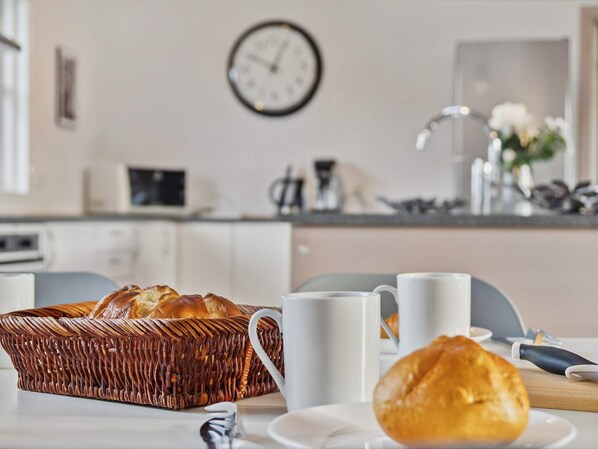 Una cocina con una cesta de mimbre para pan, tazas blancas y un reloj en la pared.