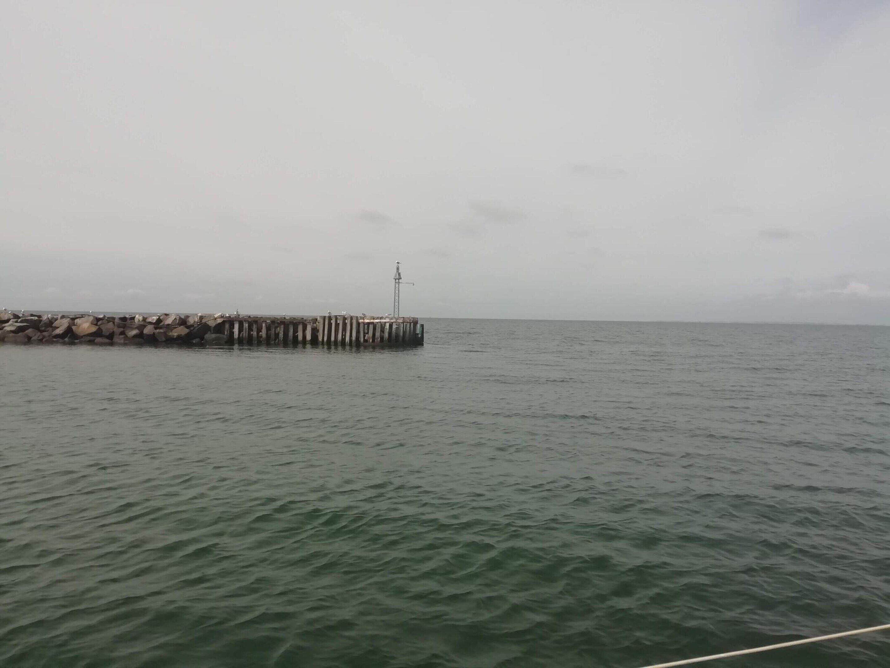 A pier extending into calm water with a weather vane on top.