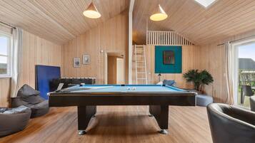 A wooden room with a pool table, two pendant lights, a blue sofa, and a ladder leading to a loft.