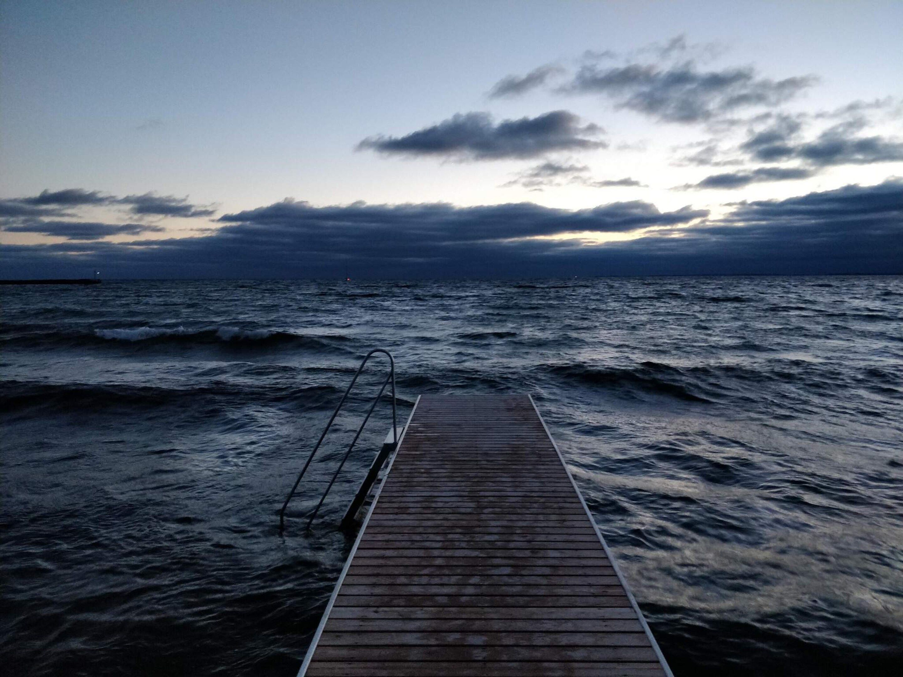 A wooden pier extending into a body of water with waves, under a cloudy sky.