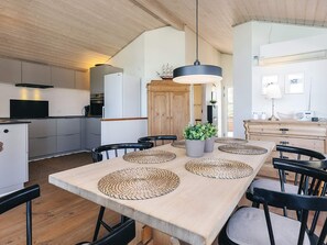 Una cocina moderna con techo de madera, comedor con una mesa larga y protectores de mesa tejidos, y un mueble de madera.