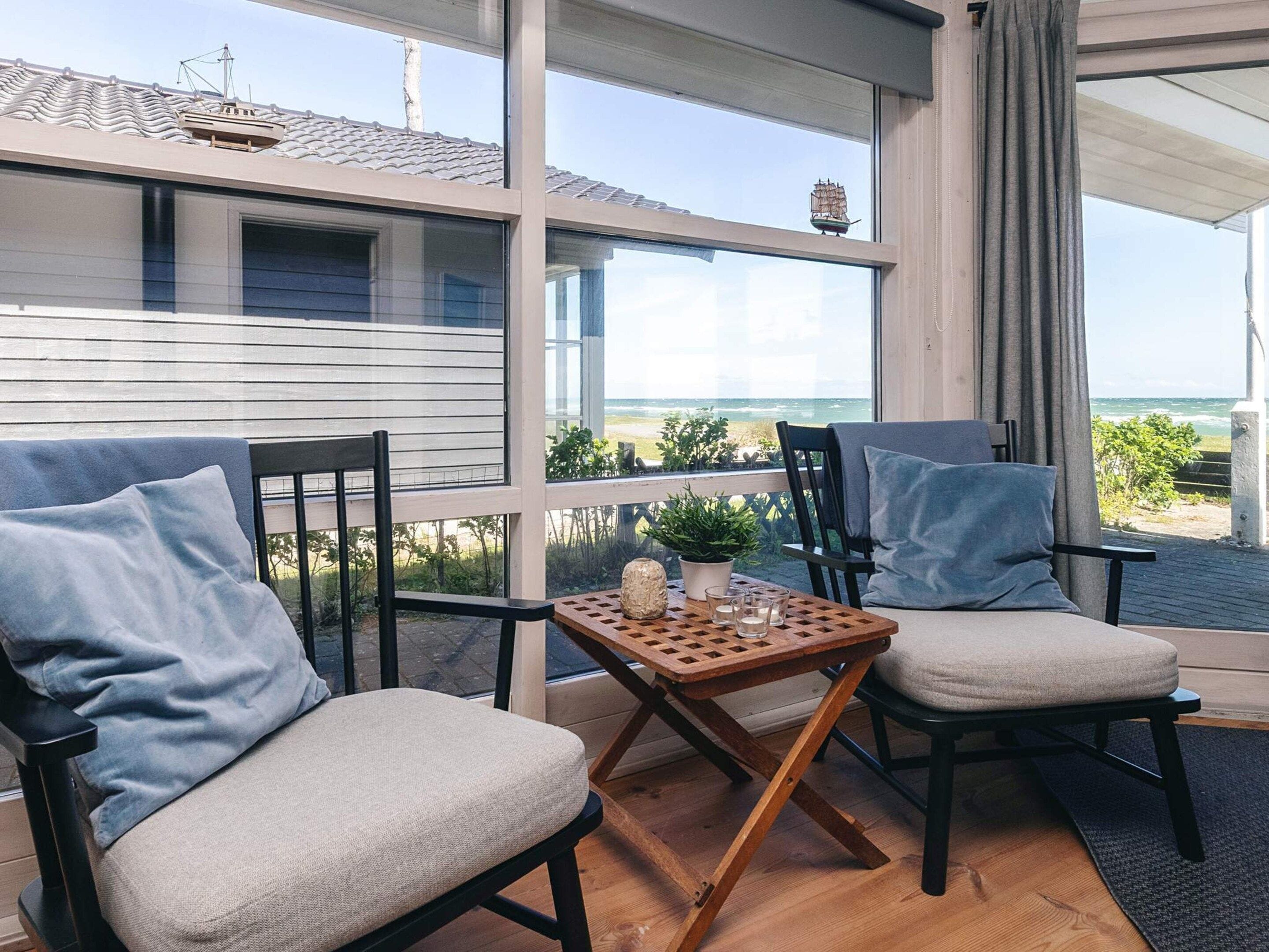 A balcony with two chairs and a small table, overlooking a coastal view.