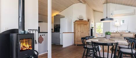 A cozy living area with a wood-burning stove, a dining table with chairs, and a kitchen in the background.
