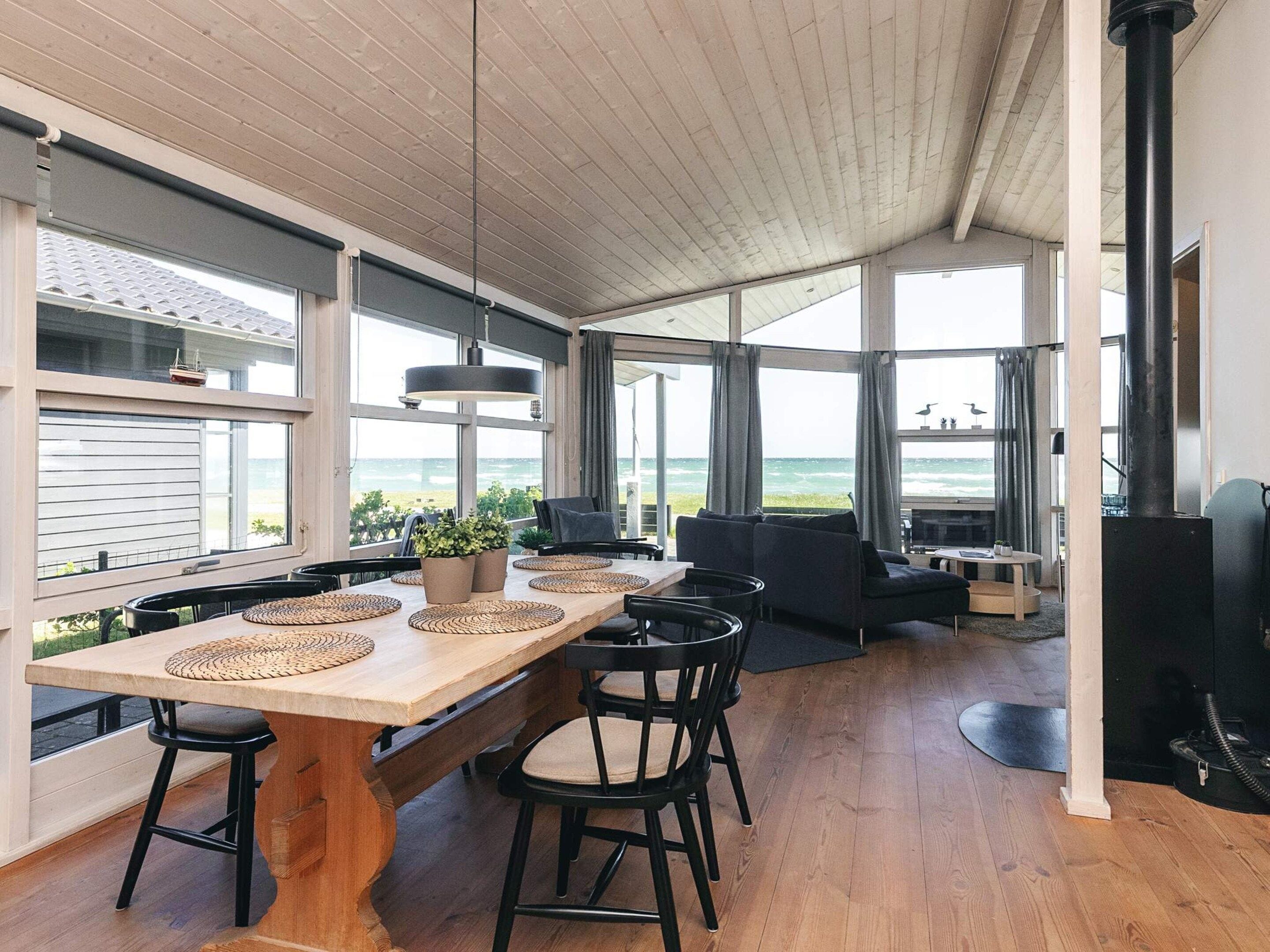A spacious living area with a wooden table and chairs, a sofa, and a large window overlooking the ocean.