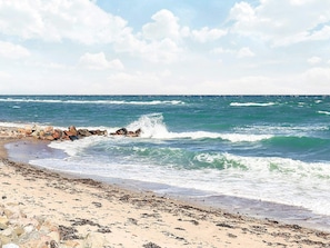 A beach with waves crashing onto the shore, a rocky breakwater, and a clear sky.