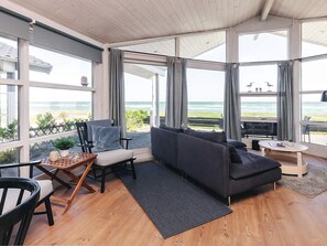 A modern living room with a large window overlooking the sea, a dark grey sofa, a wooden coffee table, and a small round table with a magazine. - Luring Holiday Home in Poljana With Sea Nearby (Otterup)