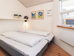 A bedroom with a bed, a shelf with books and plants, two framed pictures, and a window with a view. - Luring Holiday Home in Poljana With Sea Nearby (Otterup)