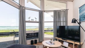 Ett modernt vardagsrum med en stor TV, bekväma sittmöbler och utsikt över havet.