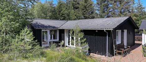 Un chalet rustique doté d’une véranda et d’une petite terrasse, entouré d’une forêt dense.