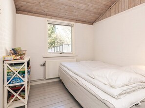 Une petite chambre avec un lit simple, un matelas blanc, une fenêtre donnant sur des arbres et un radiateur blanc.