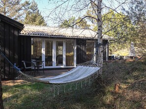 A wooden cabin with a tiled roof, a hammock, and a patio area with chairs.