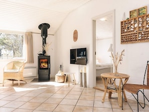 A cozy living room with a wood-burning stove, wicker furniture, a TV, and a wall-mounted shelf with decorative items. - 6 Person Holiday Home in Albaek (Aalbaek)