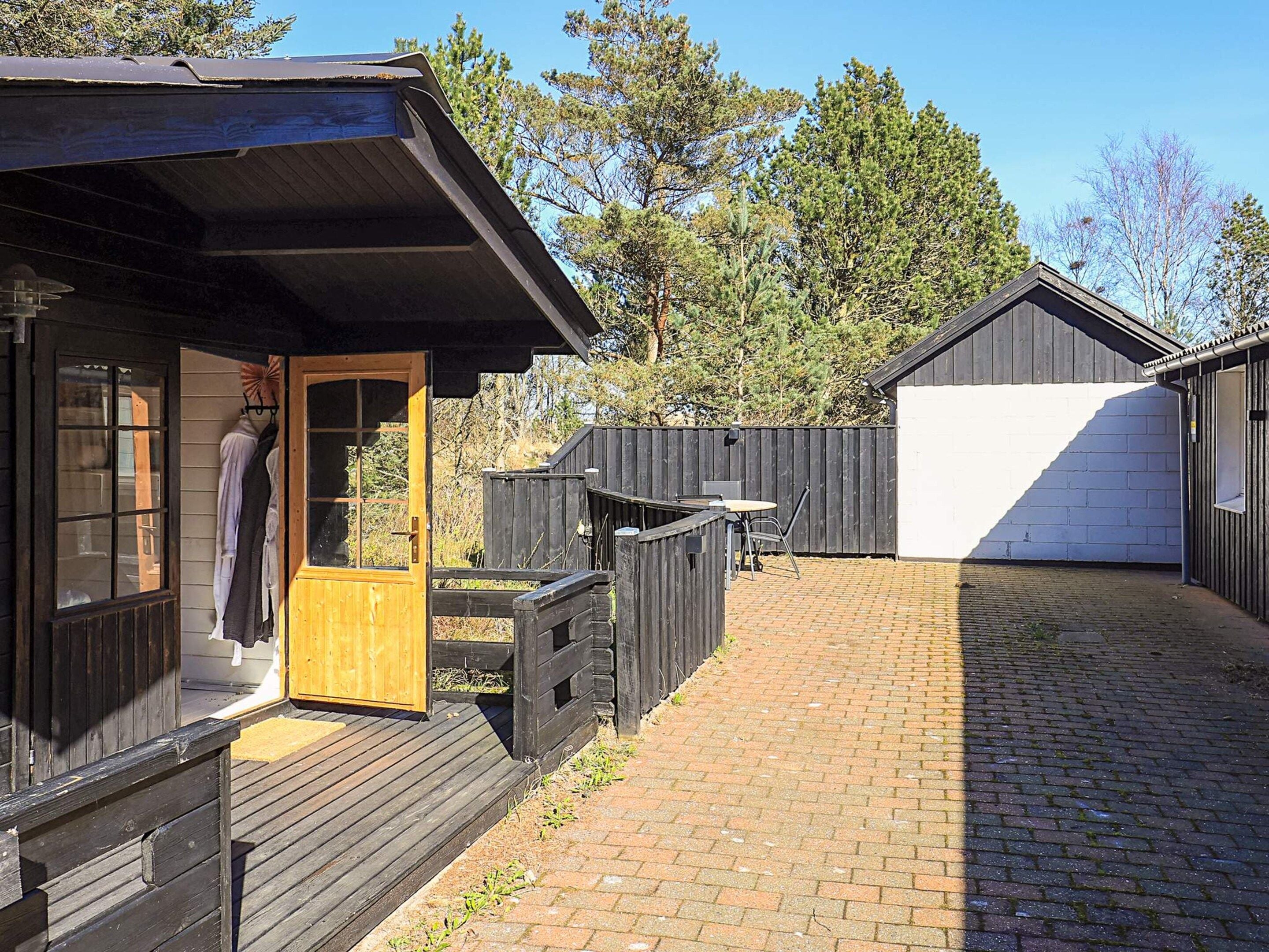 A wooden cabin with a door open, a small outdoor table, and a brick pathway.