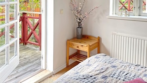 A bedroom with a bed, a small wooden table with a vase, a window with a view of a red structure, and a radiator. - Holiday Home in SÃ¶lvesborg (Sölvesborg)