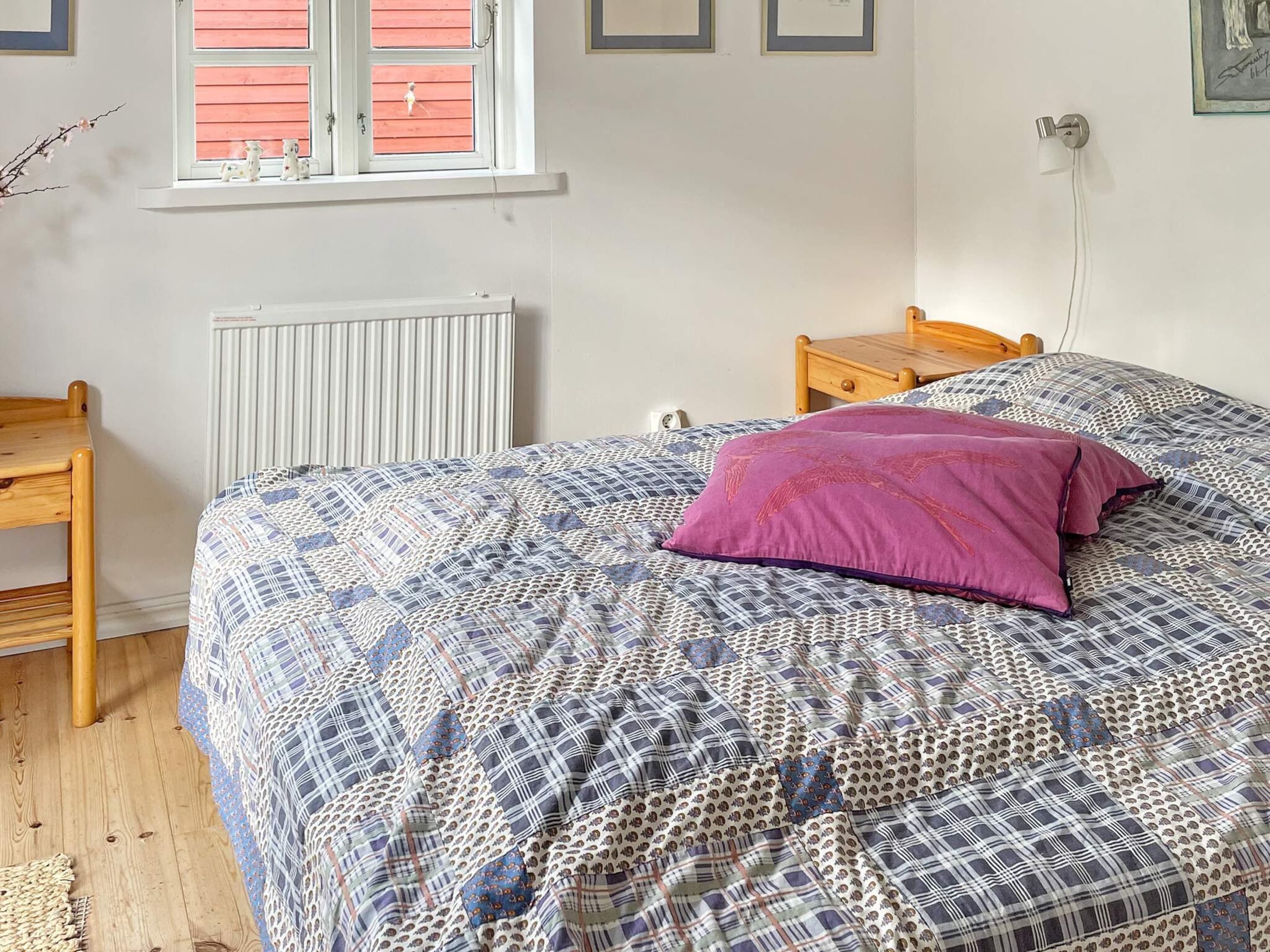 A bedroom with a bed, a wooden nightstand, a radiator, a window with shutters, and a wall-mounted lamp.