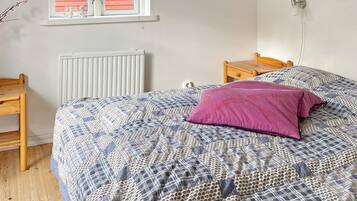 A bedroom with a bed, a wooden nightstand, a radiator, a window with shutters, and a wall-mounted lamp.