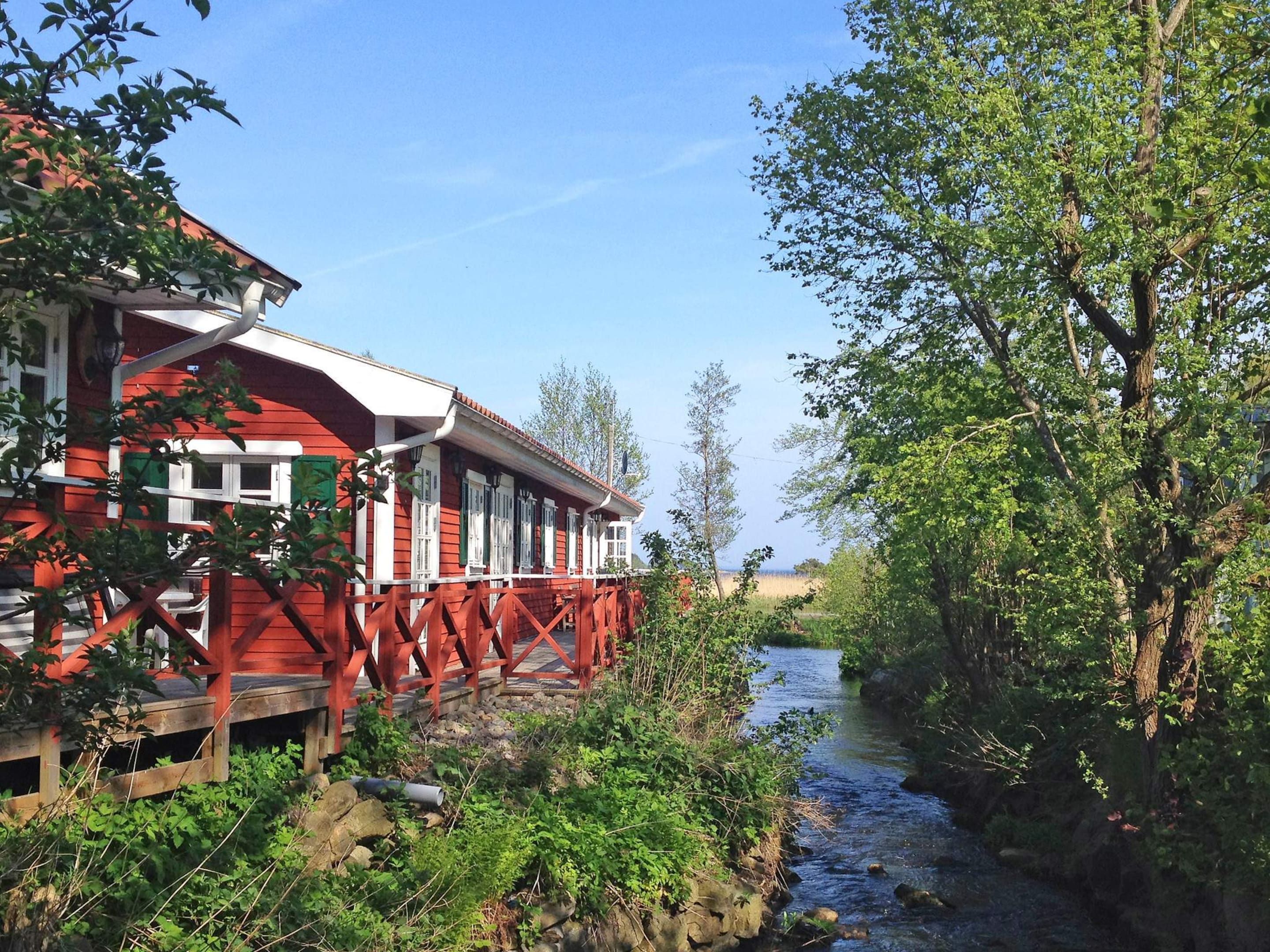 A red building with a wooden deck, a river, and greenery.