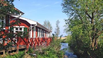 A red building with a wooden deck, a river, and greenery.