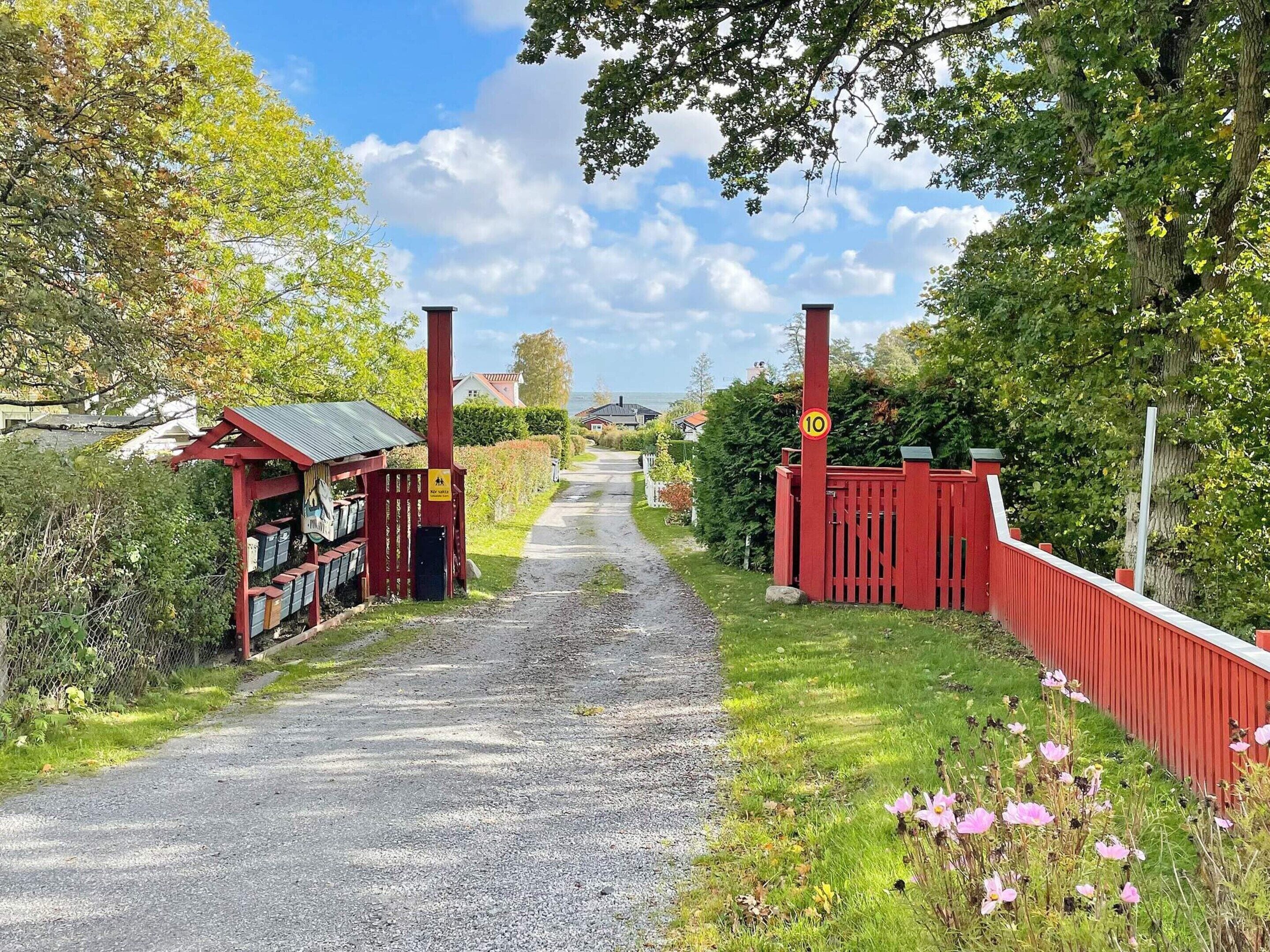 A gravel path leading to a red gate with a speed limit sign, surrounded by greenery and a small building with a red roof.