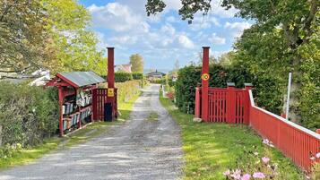 A gravel path leading to a red gate with a speed limit sign, surrounded by greenery and a small building with a red roof.