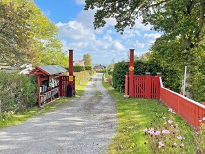 A gravel path leading to a red gate with a speed limit sign, surrounded by greenery and a small building with a red roof. - Holiday Home in SÃ¶lvesborg (Sölvesborg)