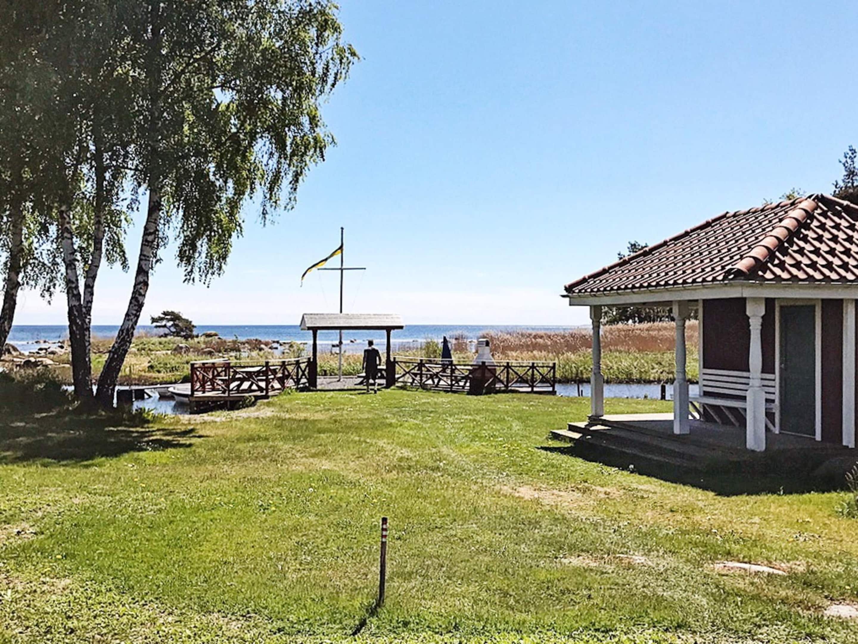 A gazebo with a tiled roof, a flagpole with a flag, and a grassy area with a view of the water.