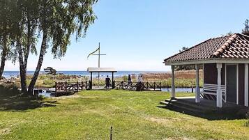 A gazebo with a tiled roof, a flagpole with a flag, and a grassy area with a view of the water.