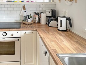 Een keuken met een witte kookplaat, een houten aanrecht, een Bosch koffiezetapparaat en een spoelbak.