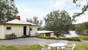 A small house with a gravel driveway, a wooden bench, and a table with chairs in front.